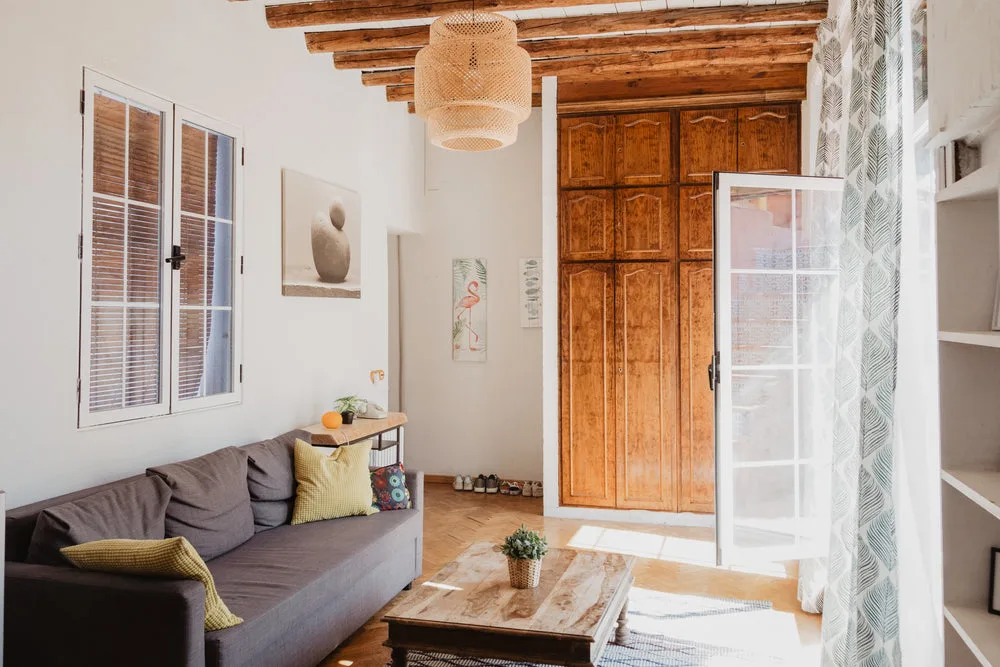 A warm living room with timber furniture, natural light, and a woven lampshade