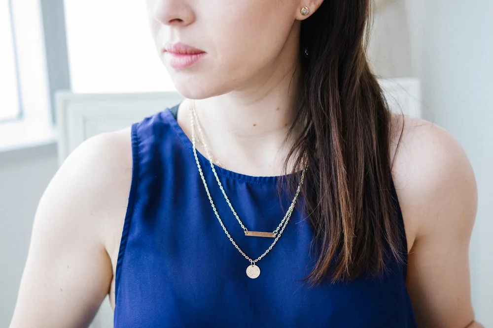 Layered gold-tone necklaces worn over a deep blue top
